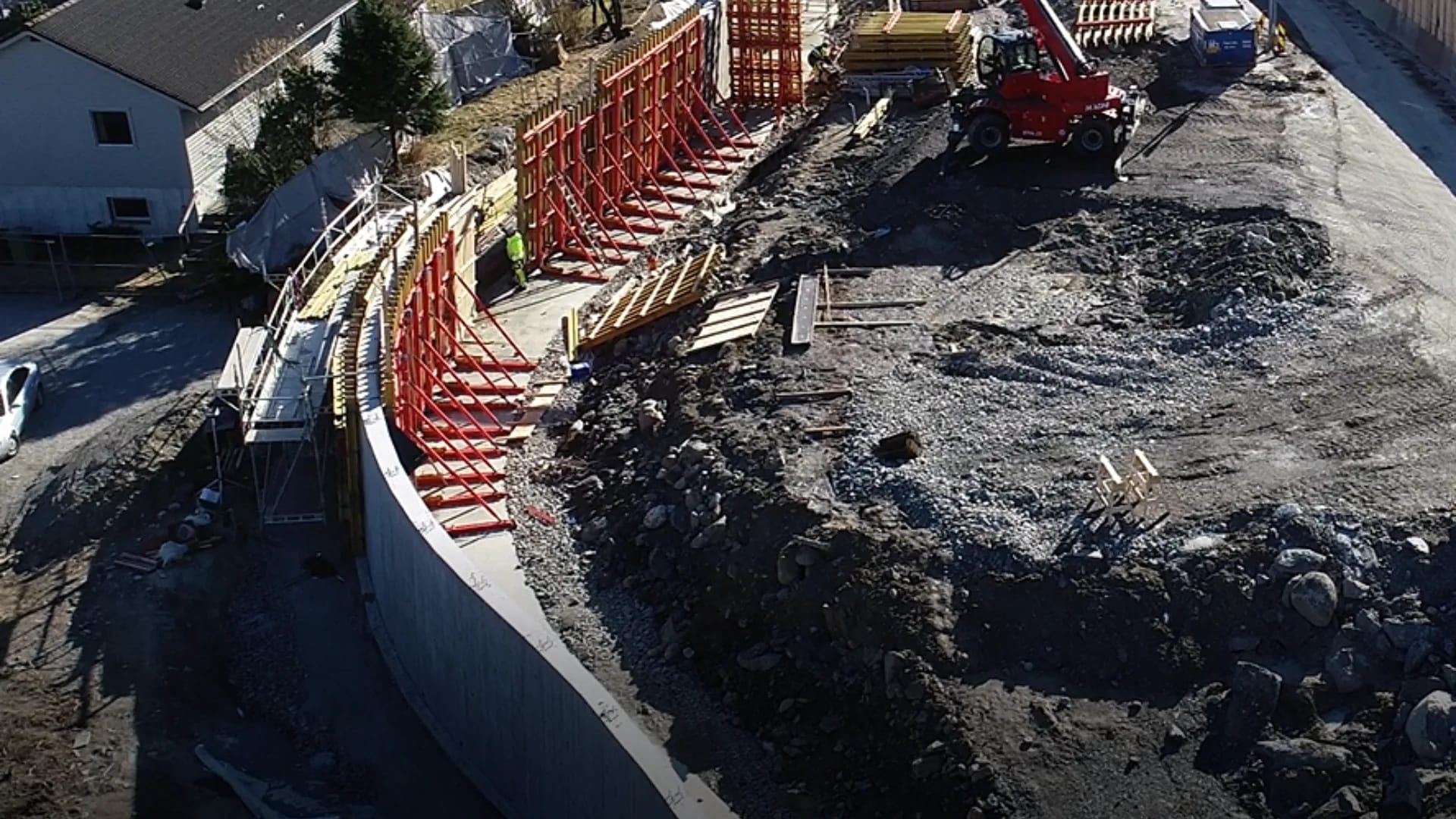 Støttemur i betong med rød systemforskaling langs veitrasé.